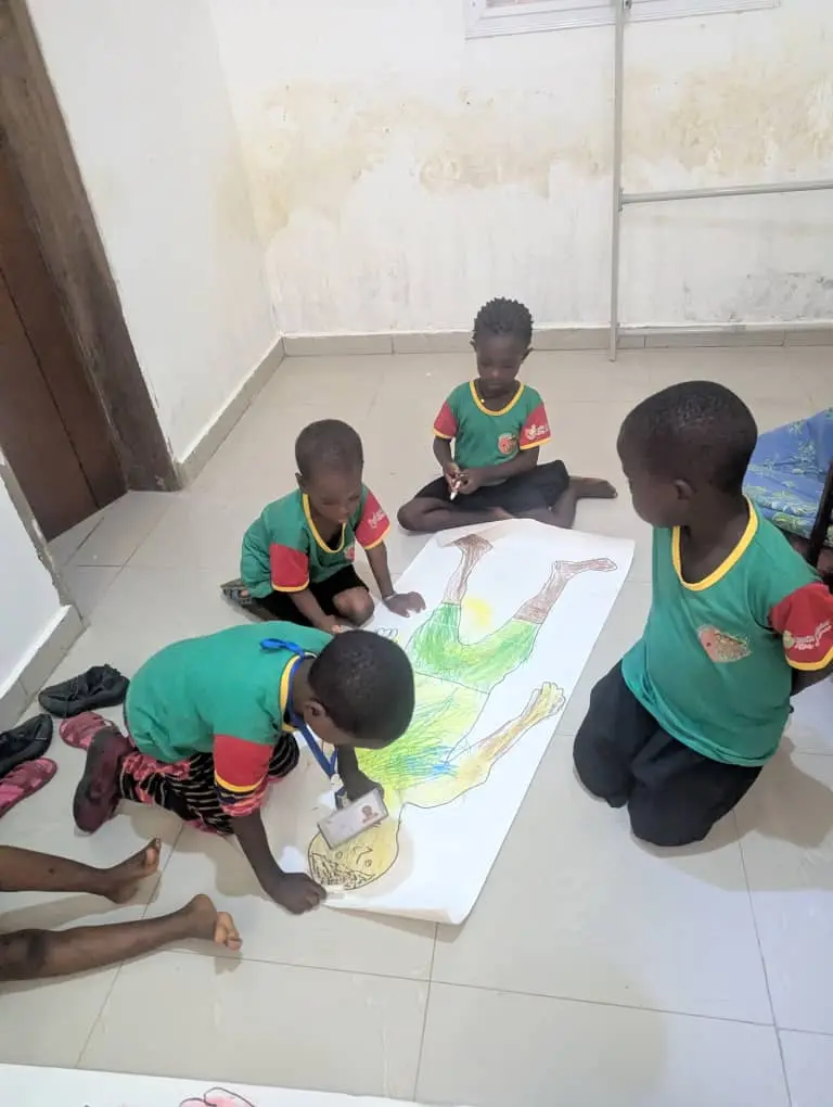 Crianças ajoelhadas no chão colorindo um mural de papel em grupo