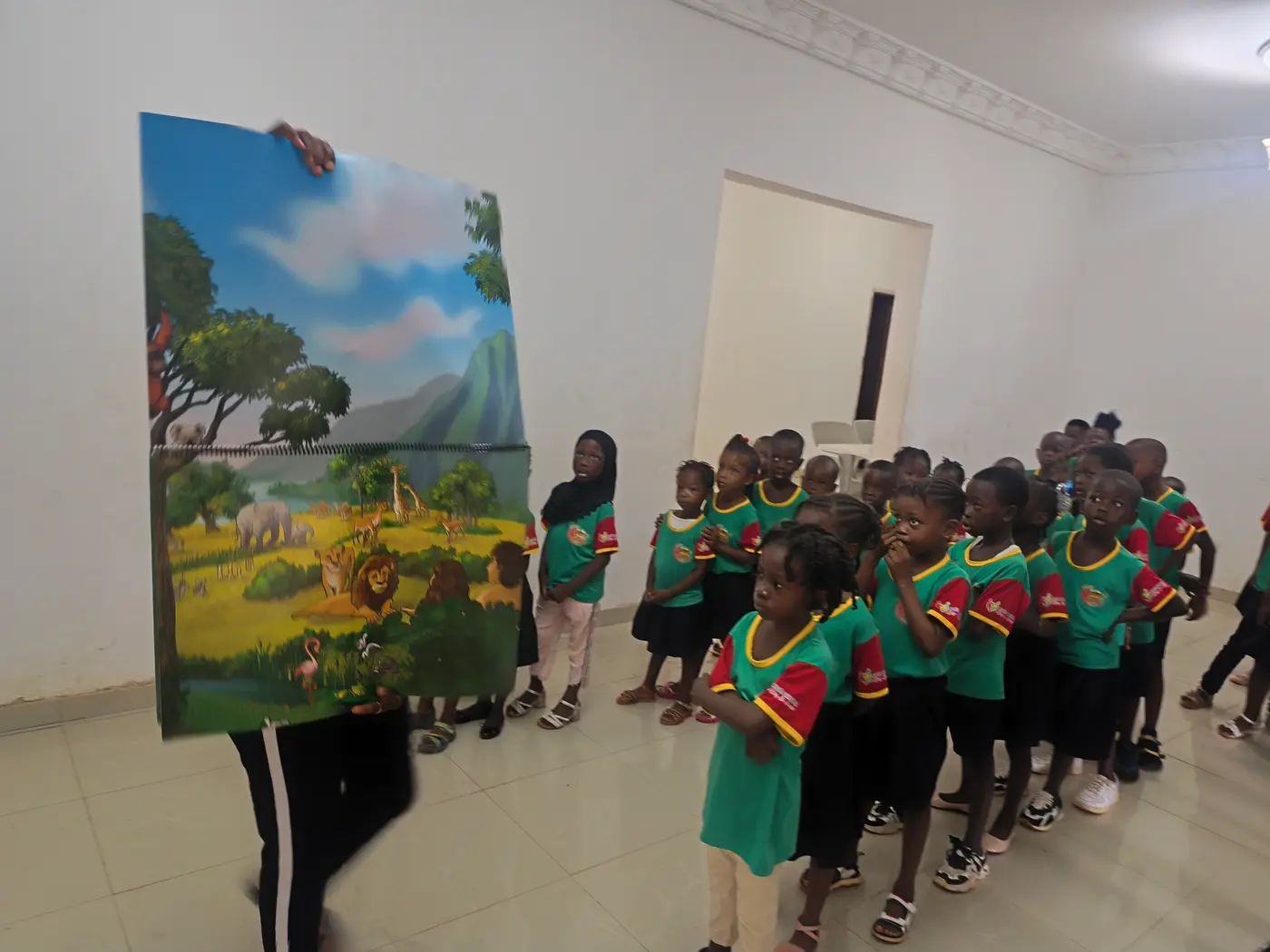 Adulto segurando um painel ilustrado de animais da savana para uma fila de crianças