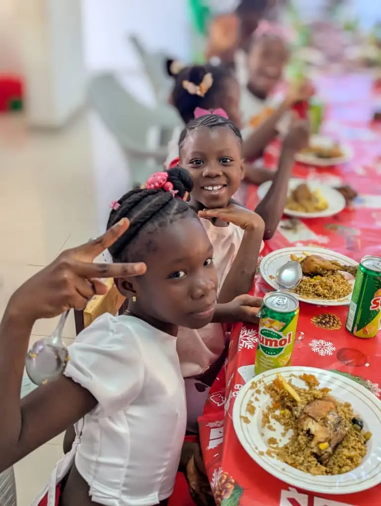 Duas meninas fazendo sinal de positivo com a mão à mesa de Natal, pratos de arroz com frango